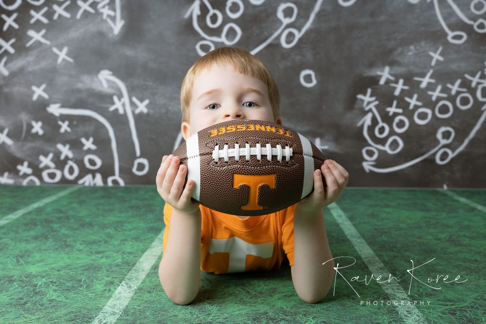 Boy posing with University of Tennessee Volunteers football for themed studio portrait session