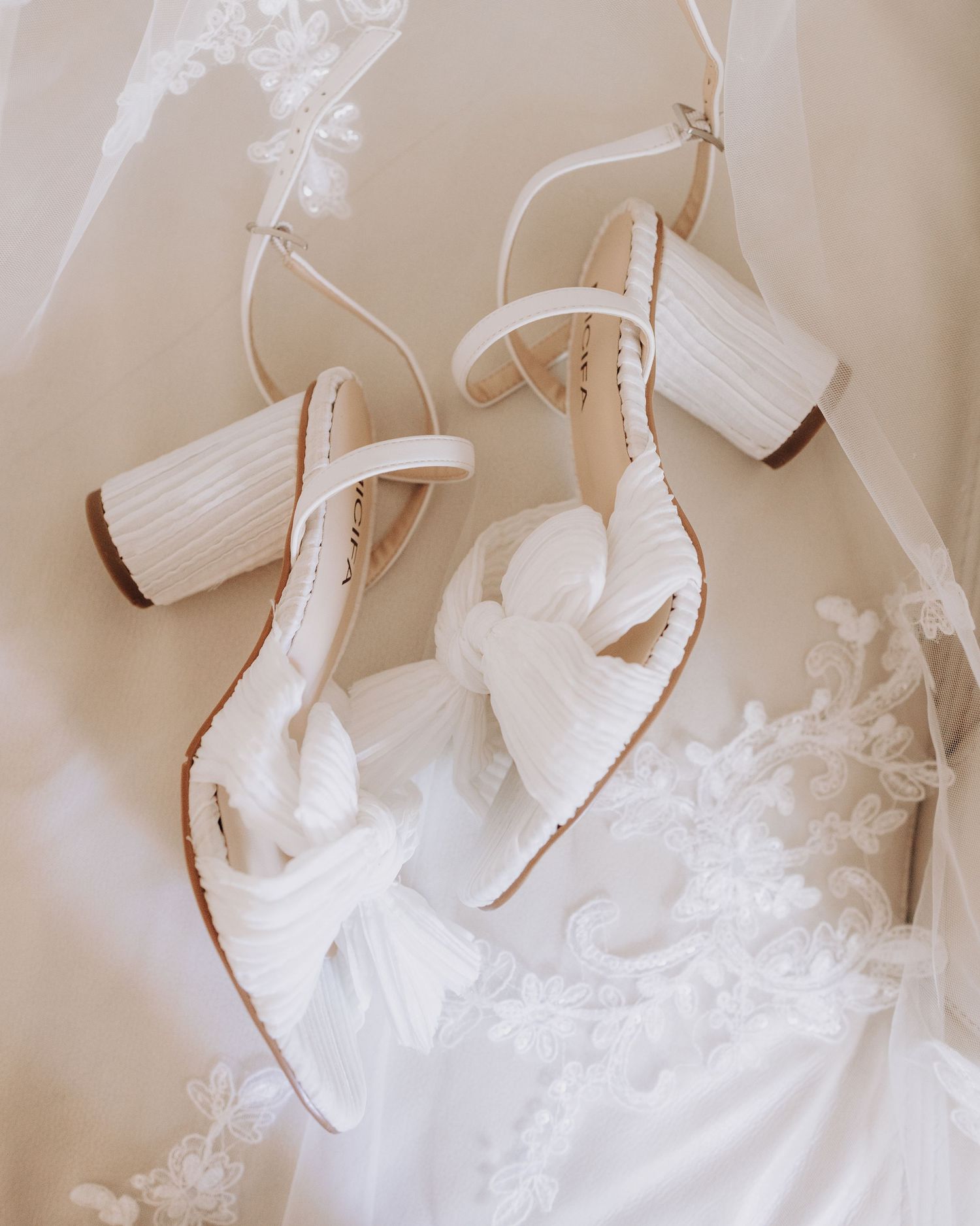 White block heel wedding sandals hanging with lace details in the background.