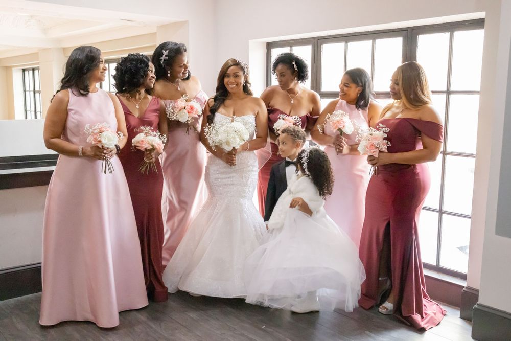 Wedding party poses together with bridesmaids wearing pink and burgundy dresses alongside bride in white gown.