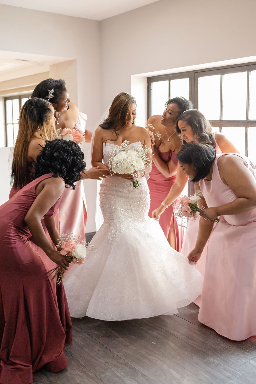 Bridesmaids in pink dresses admire bride's white mermaid wedding gown.