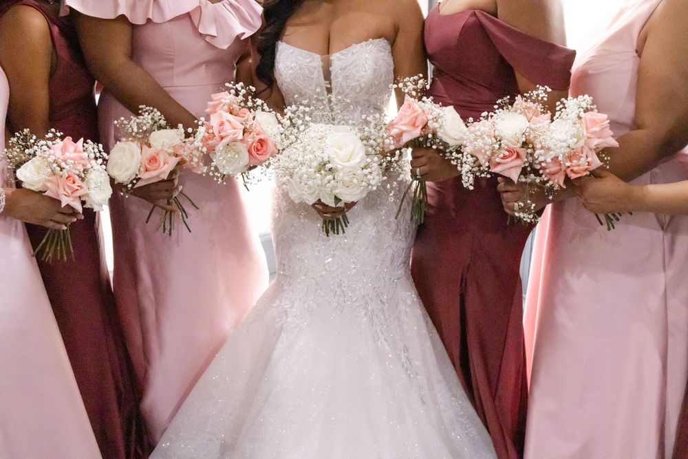 Close-up of wedding bouquets in white and blush pink against bridal party dresses.