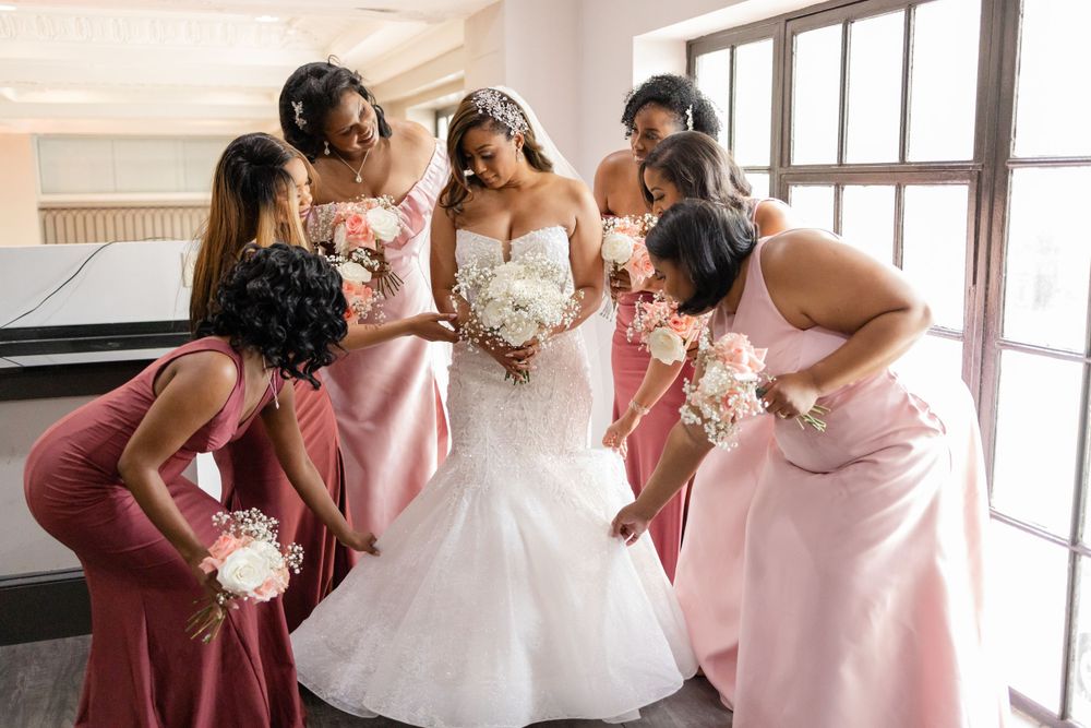 Wedding party in pink dresses circles around bride holding white bouquet.