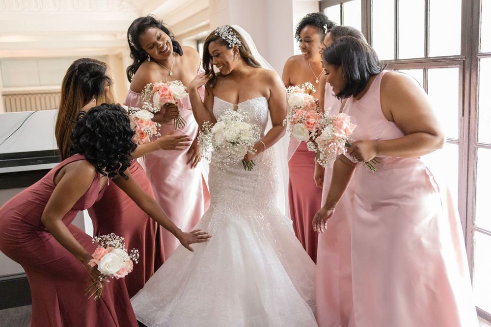Wedding party in pink dresses gathers around bride in white gown.