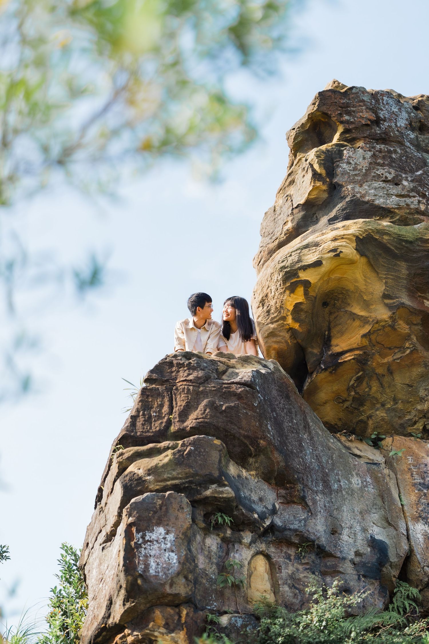 Two people sitting atop a dramatic rock formation against a blue sky.
