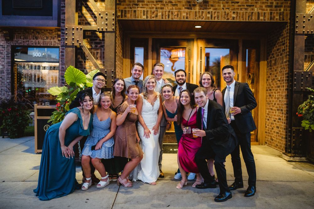 A wedding party poses together outside a brick building entrance.