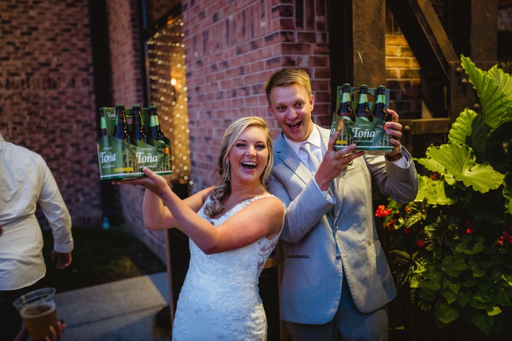 A couple in wedding attire enjoys celebratory drinks together at a brick-walled venue.