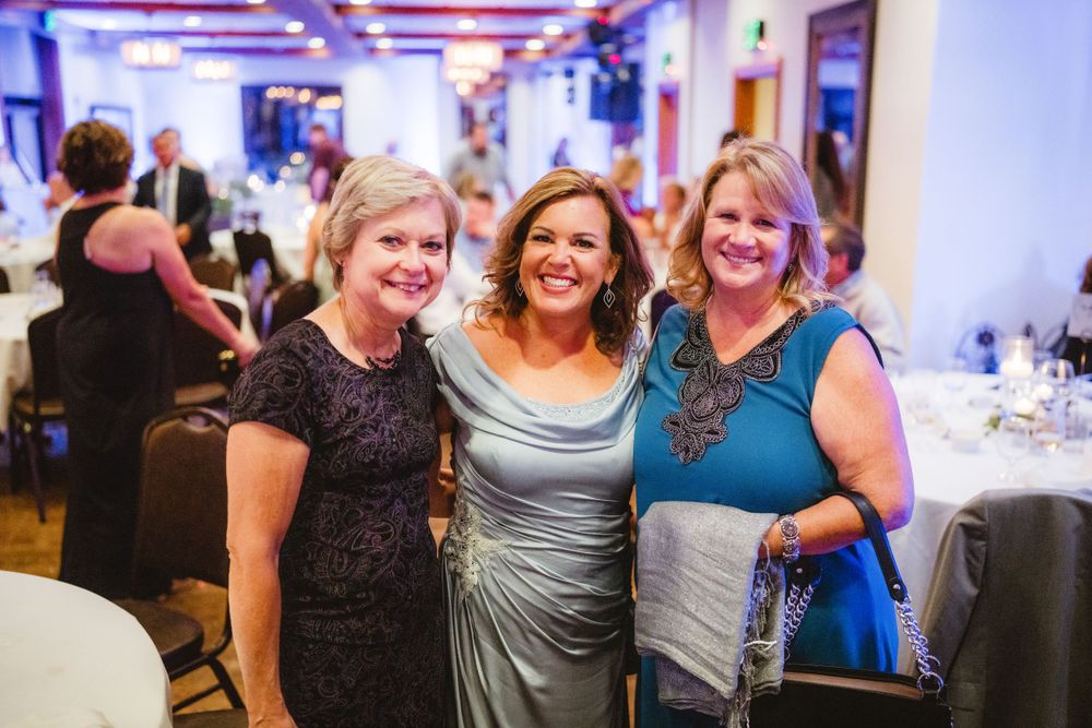 Three women in formal attire pose together at an evening wedding reception.
