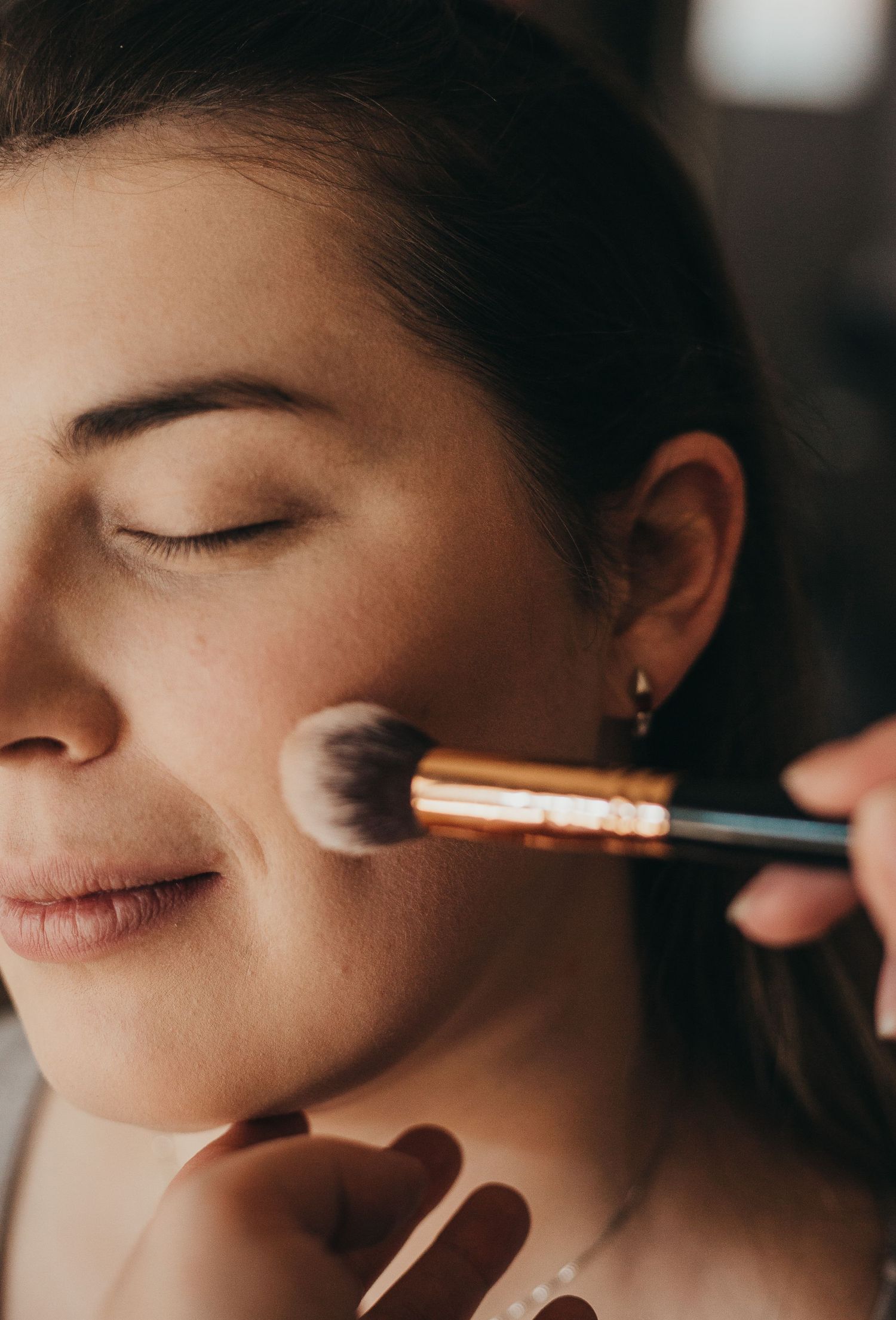 Close-up profile shot of makeup application using a fluffy brush on cheeks.