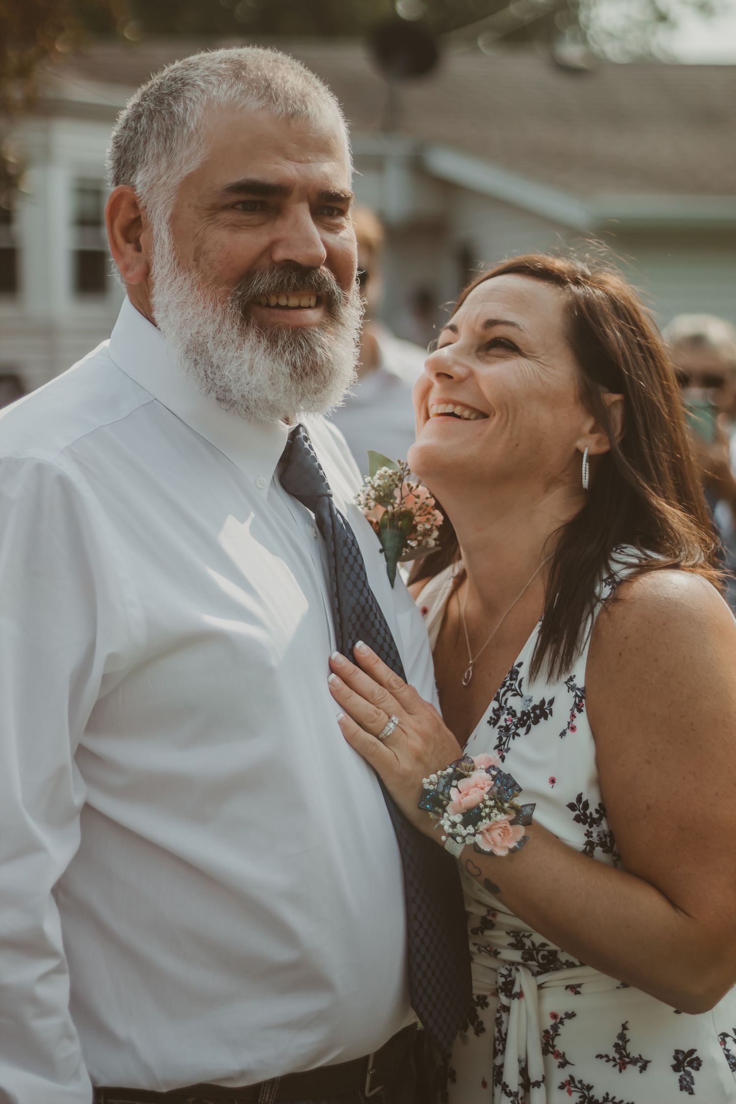 A happy couple at a wedding celebration, with the man in white and woman in floral dress.