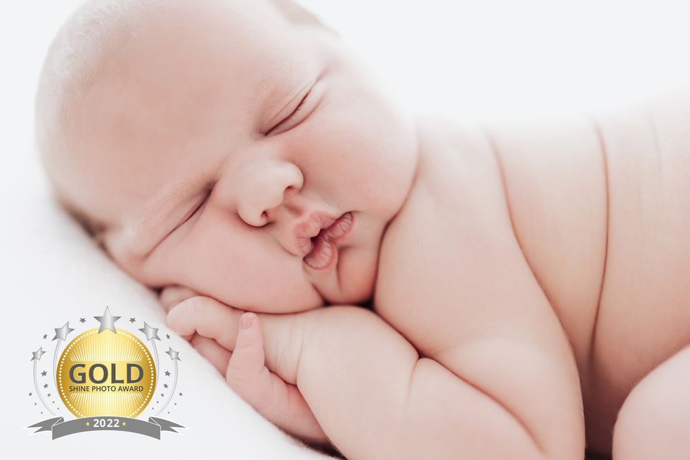 Peaceful sleeping newborn with gold award badge on white background.