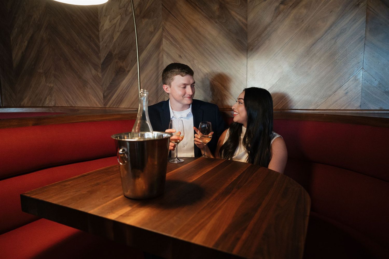 Couple sharing an intimate moment in a dimly lit restaurant booth with wine.