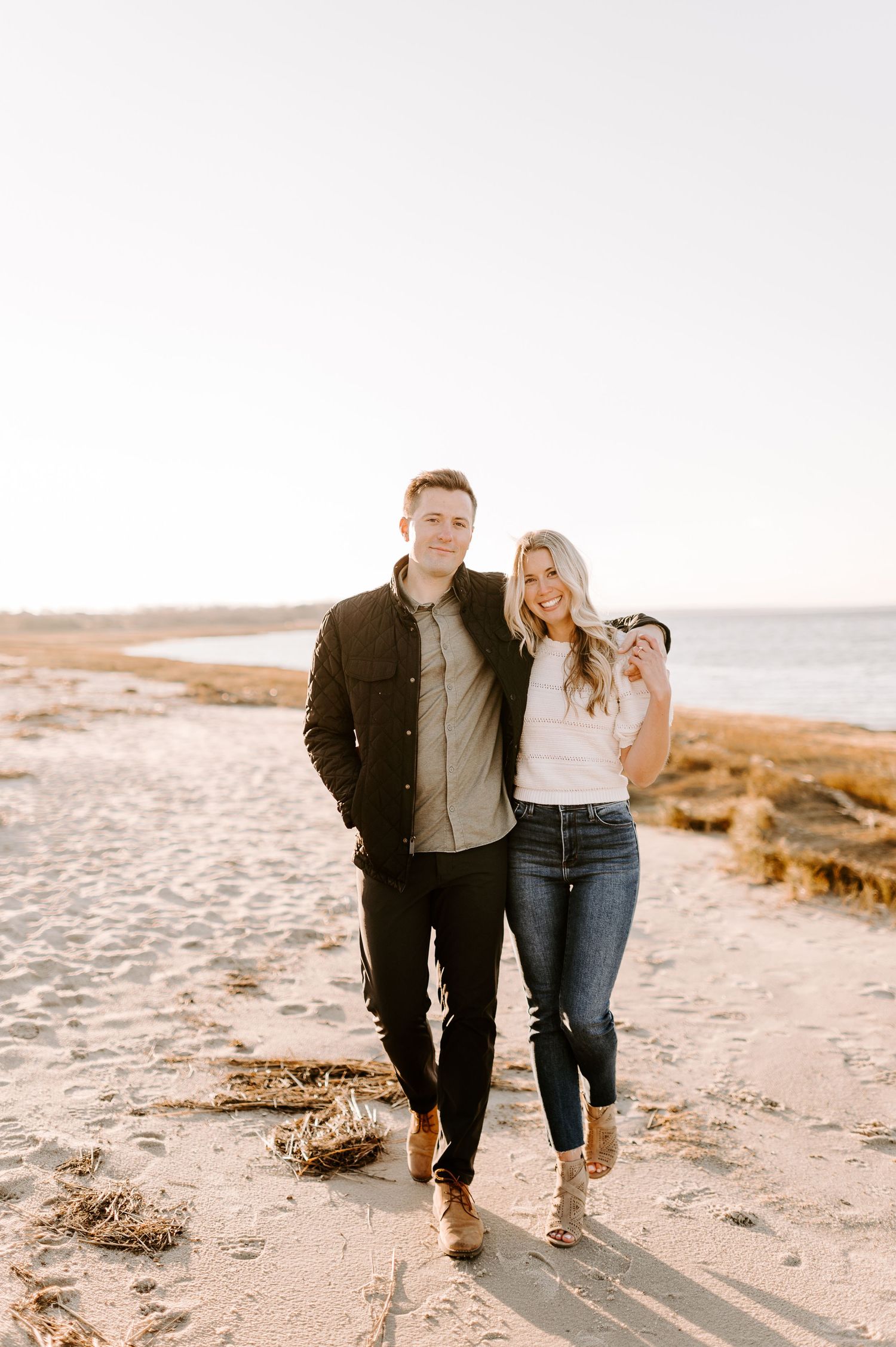 Couple walking hand in hand along scenic coastal beach at sunset.