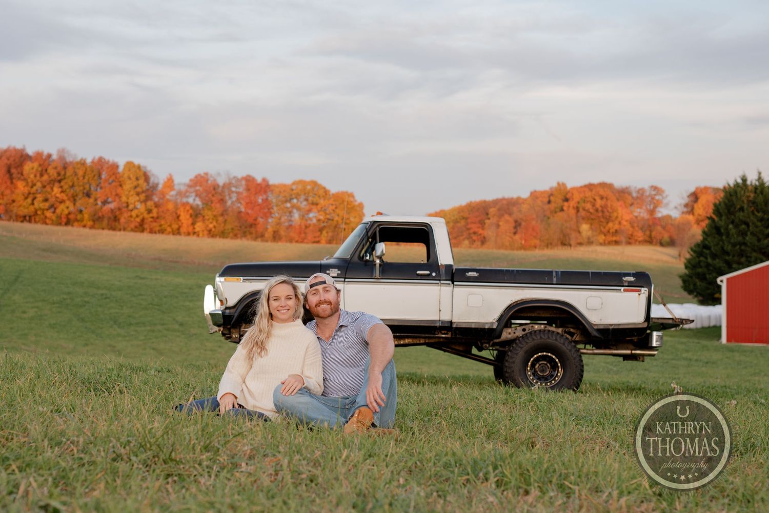 Countryside engagement photo with classic lifted Ford pickup truck against fall foliage.
