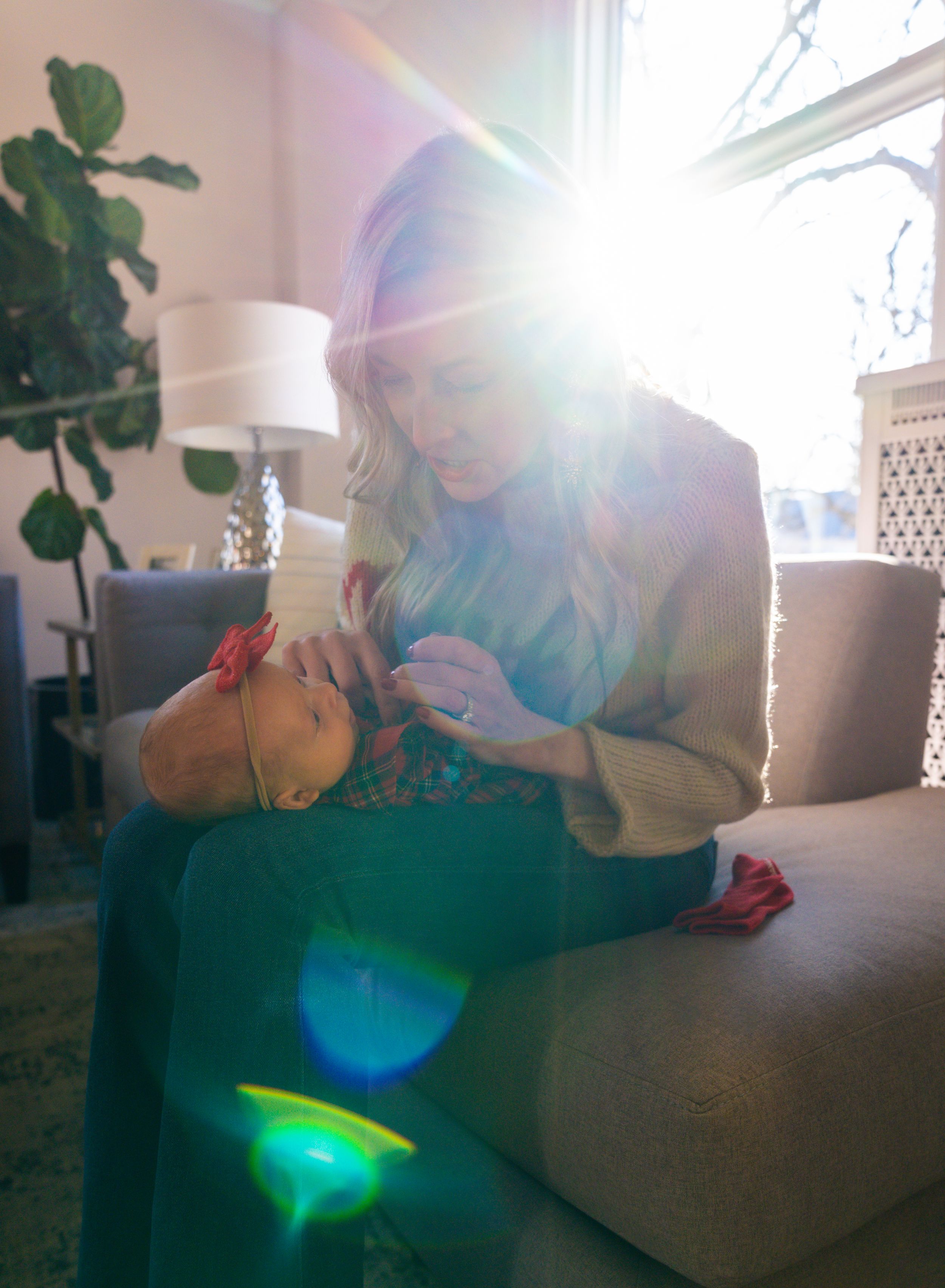 Sunlit indoor portrait showing caregiver tending to infant with lens flare through window.