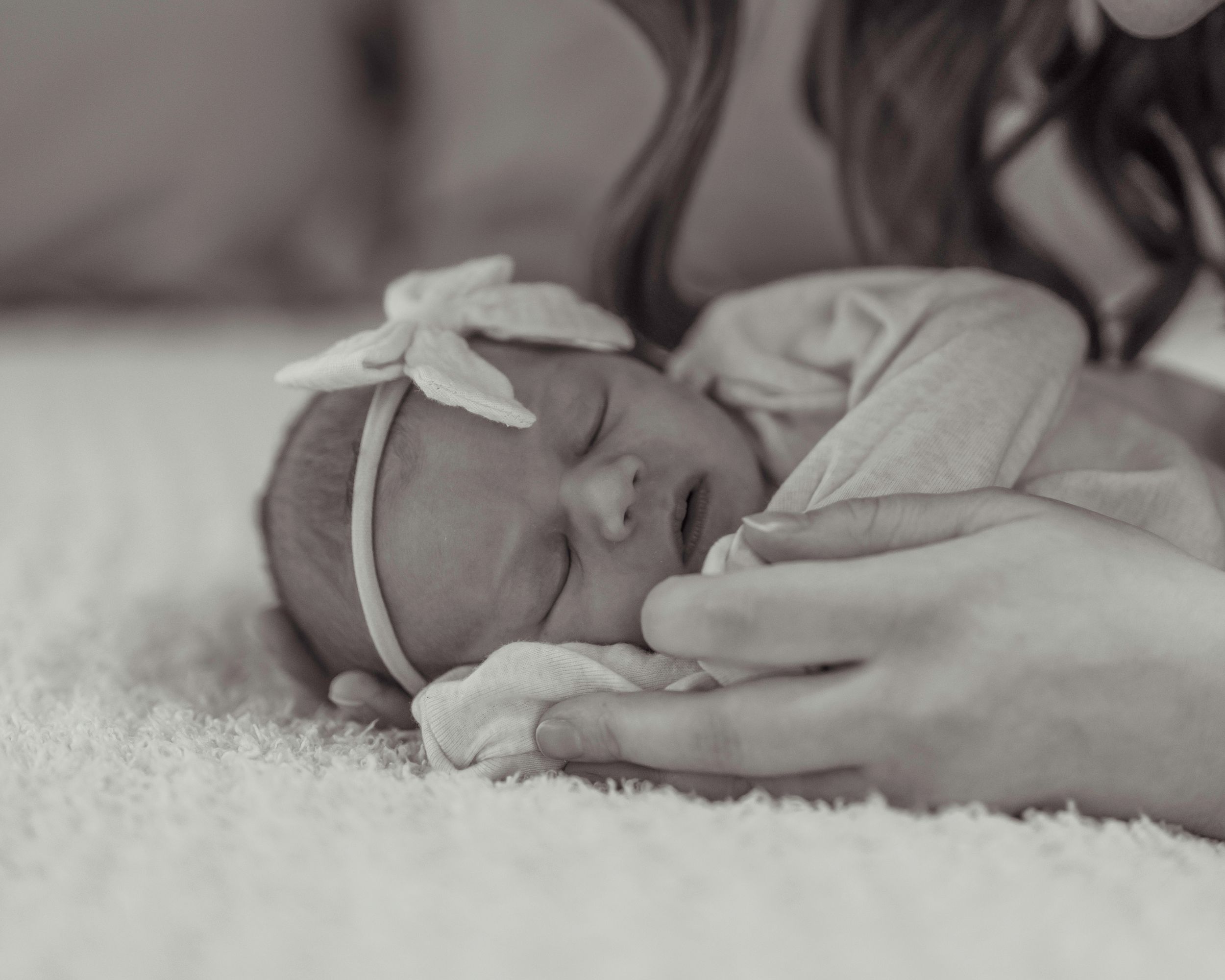 Black and white newborn photography of sleeping baby with headband on soft blanket.