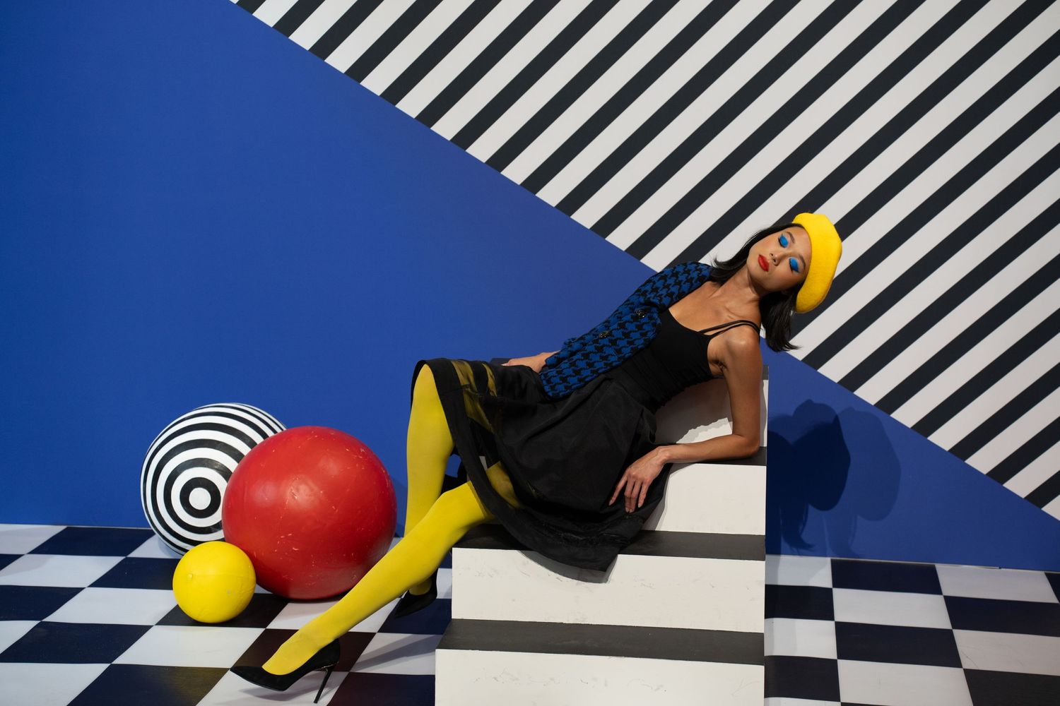 Artistic fashion shoot with black and yellow outfits against geometric striped background and checkered floor.