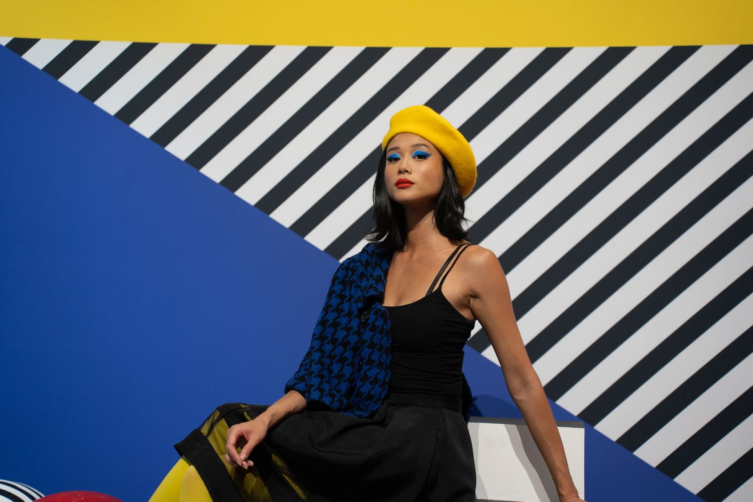 Modern fashion photography featuring bold yellow and blue colors with diagonal stripes and geometric elements.