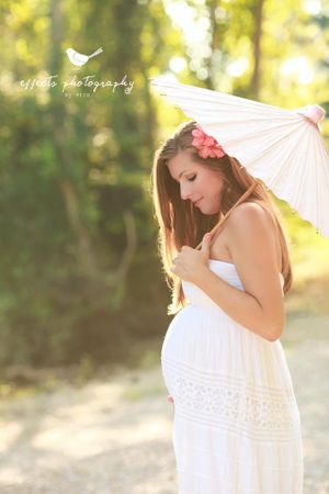Dreamy maternity portrait with parasol in golden sunlight and flowing white dress.