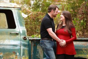 Couple in casual attire posing by vintage blue truck during maternity photo shoot.