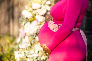Close-up of a pink maternity dress with roses in soft natural lighting.