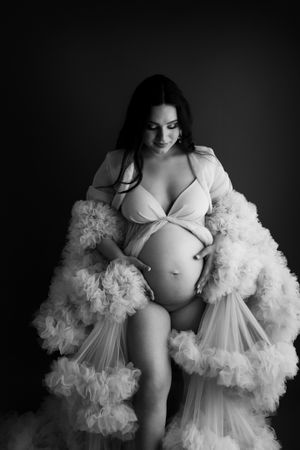Dramatic black and white maternity portrait with voluminous white ruffled robe.