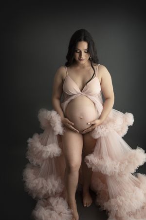 Intimate maternity portrait featuring soft pink ruffled robe against dark background.