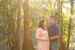 Couple embraces during sunset maternity photo session in wooded area.