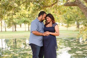 Couple shares intimate moment during maternity photo session by pond.