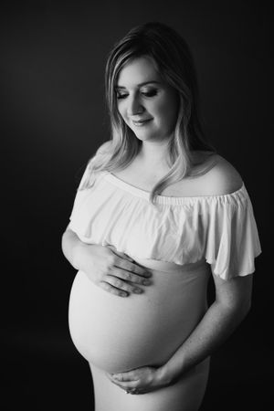 Black and white maternity portrait showing gentle moment with off-shoulder gown.