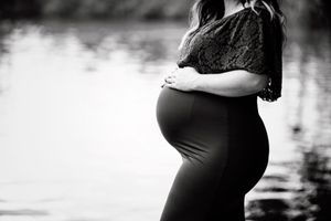 Black and white silhouette of pregnant figure in lace dress by water.