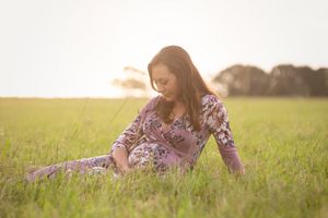 Maternity portrait in floral dress amid golden sunlit field.