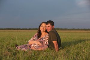 Intimate maternity portrait of couple sitting in grassy field at dusk.