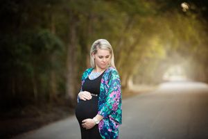 Maternity portrait of an expectant mother wearing a colorful floral kimono standing on a tree-lined path.