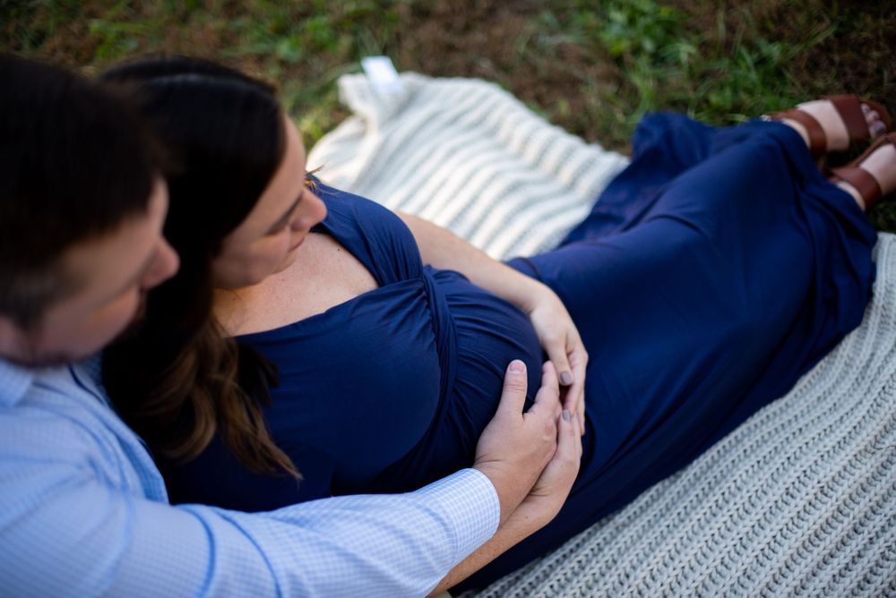 A couple on a blanket looking down at her pregnant stomach
