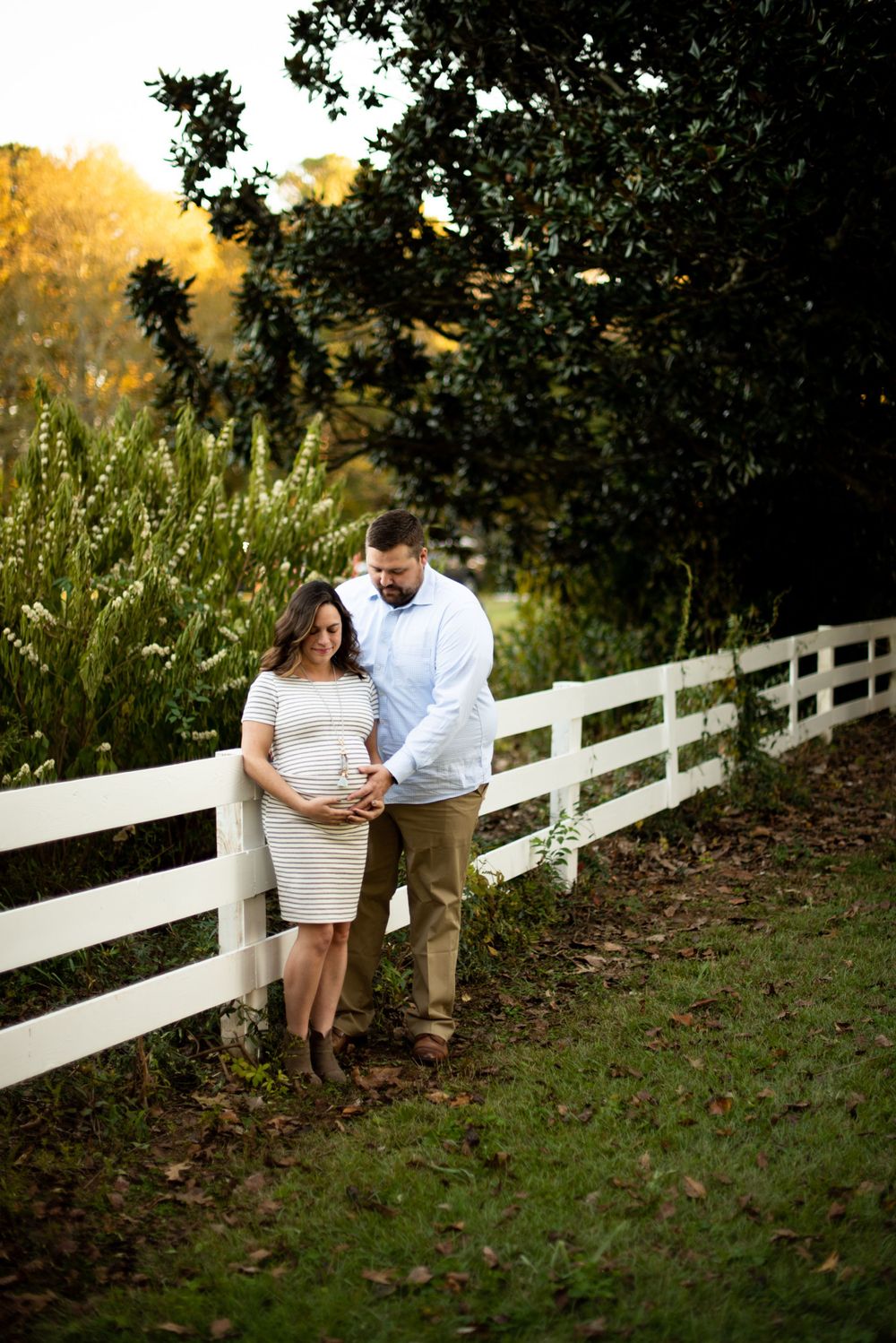 A couple standing next to fence looking down on the wife's pregnant stomach