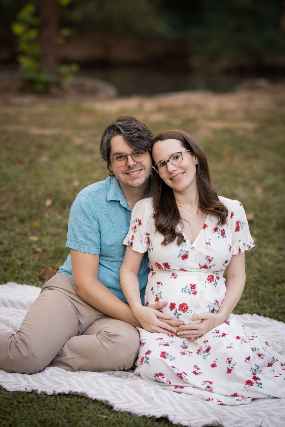 A husband and wife snuggling on a blanket. She's pregnant