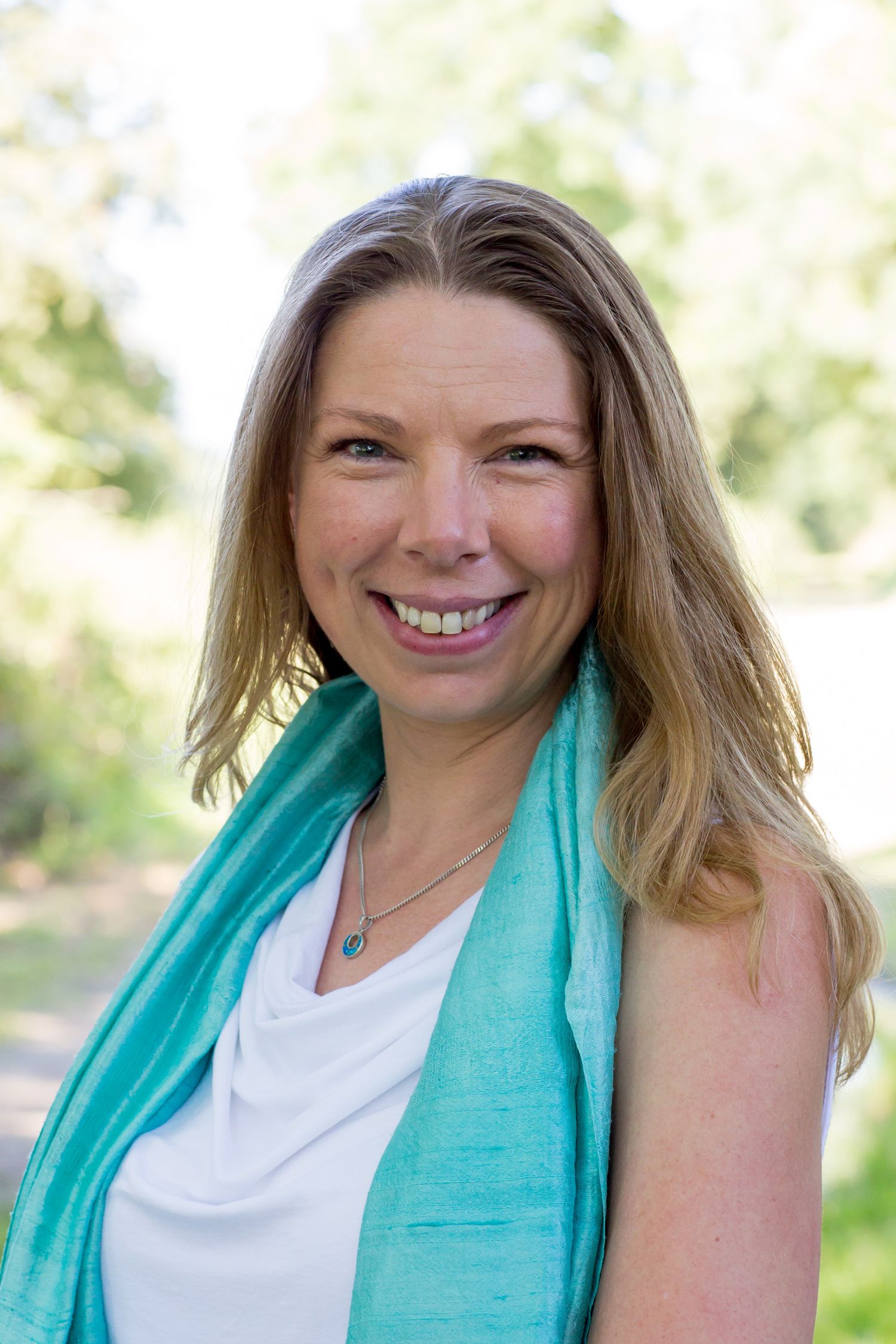 Portrait of a person in a white top and turquoise scarf smiling outdoors during business branding photoshoot.