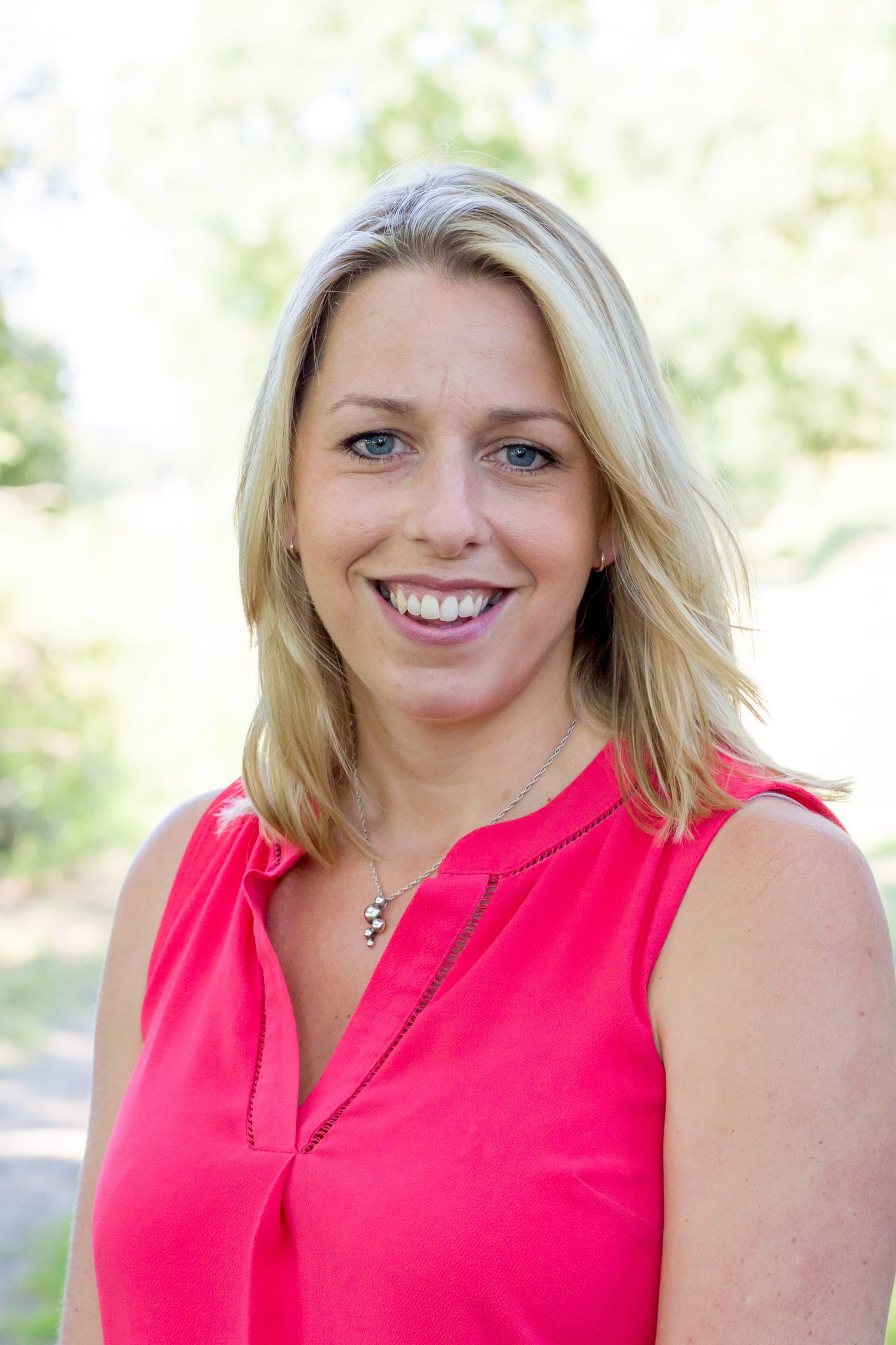 Professional headshot of a person wearing a coral sleeveless top against a natural background during business branding photoshoot.