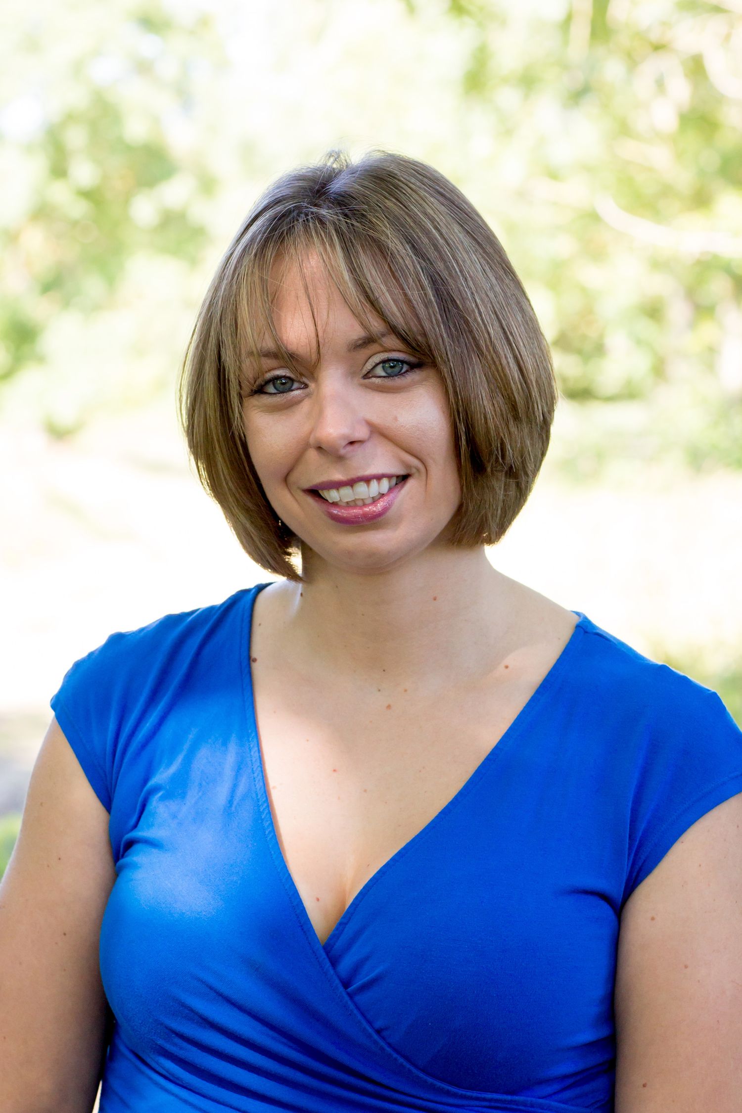 Portrait of a person in a blue v-neck top with short brown hair smiling at the camera during business branding photoshoot.