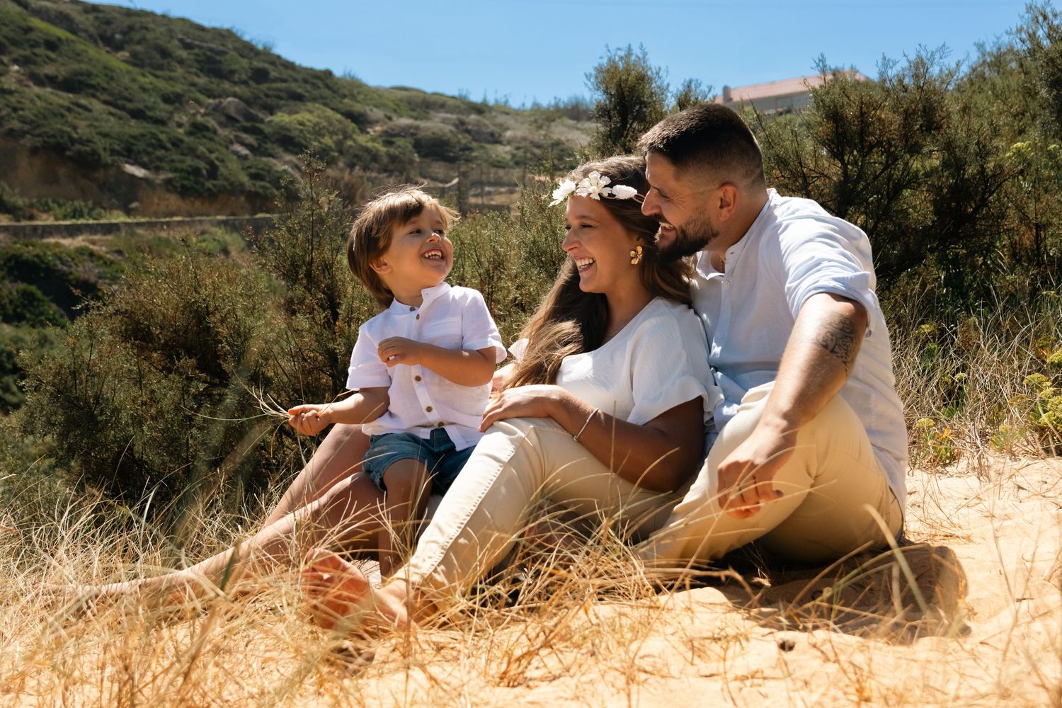 Family enjoying time together on sunny hillside with coastal vegetation.