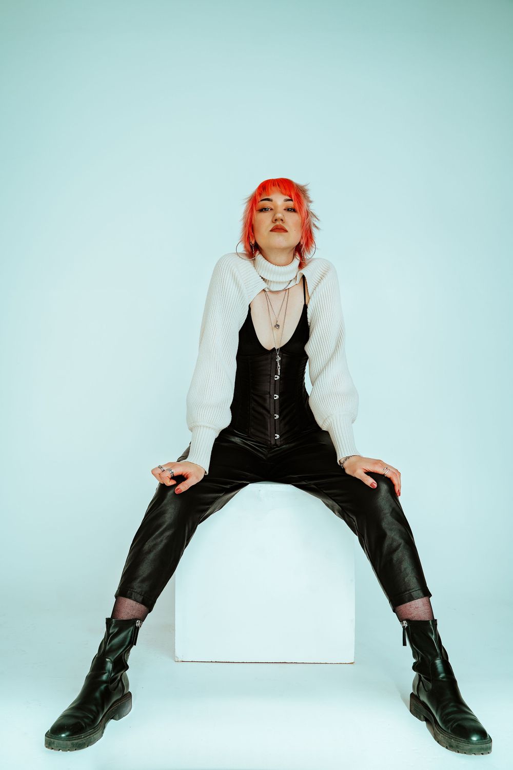 Studio portrait with minimalist white backdrop featuring black vest and boots outfit.