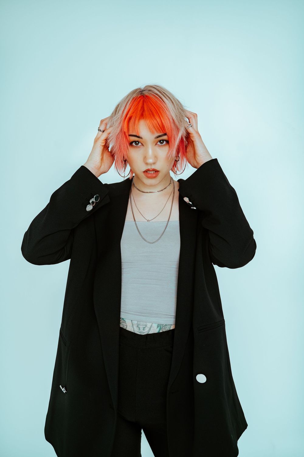 Fashion portrait with bright orange hair against light blue studio background.