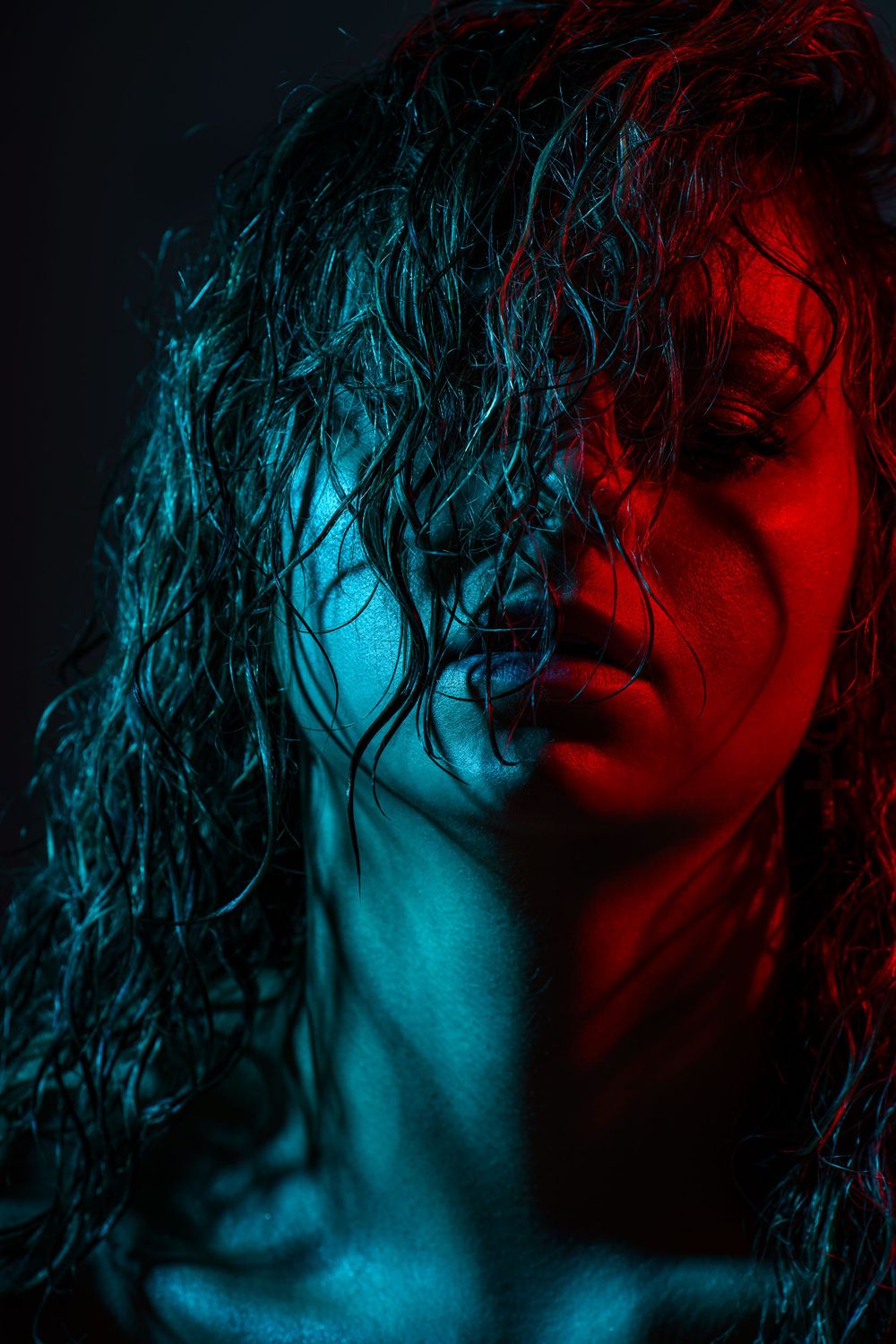 Artistic portrait with wet hair effect under blue and red lighting creates dramatic mood.