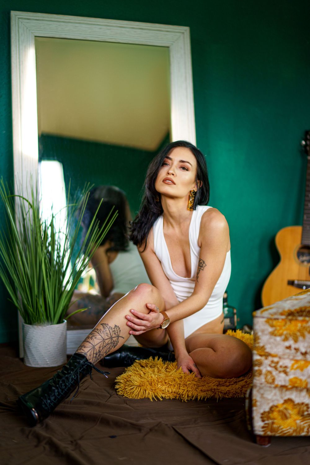 Bedroom photoshoot with white tank top and boots against teal walls and yellow accents.