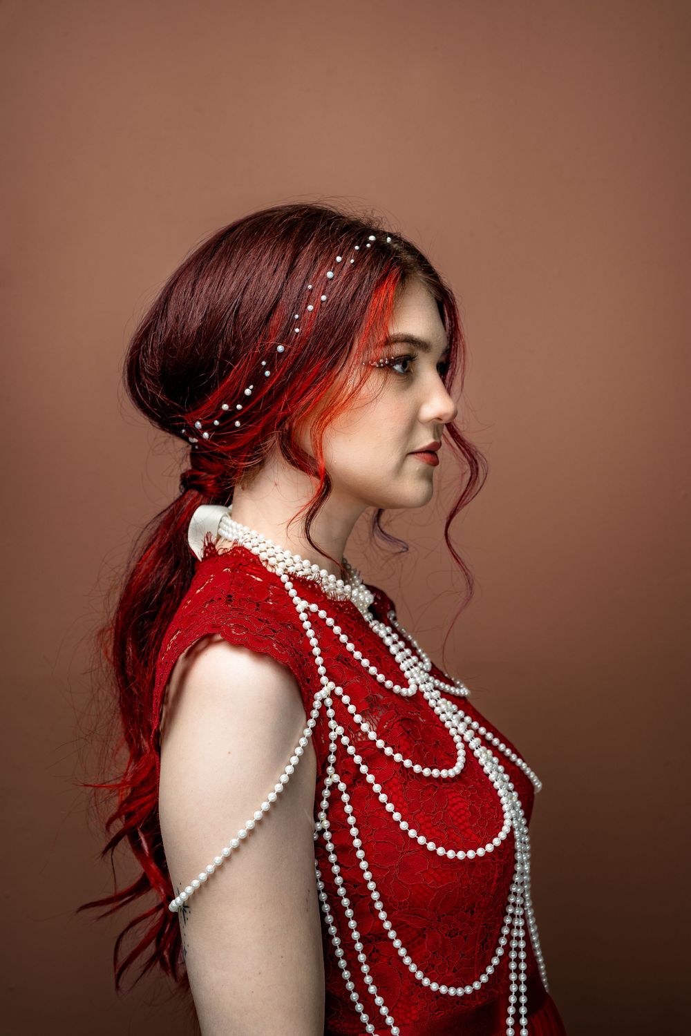 Artistic portrait series featuring red hair and draped pearl necklaces against a dark brown background.