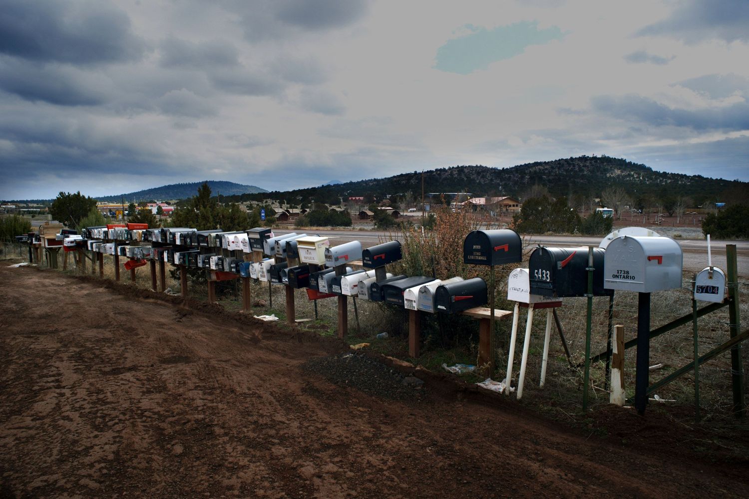 Une rangée de boîtes aux lettres rurales aux États Unis borde un chemin de terre sur fond de montagne nuageux.