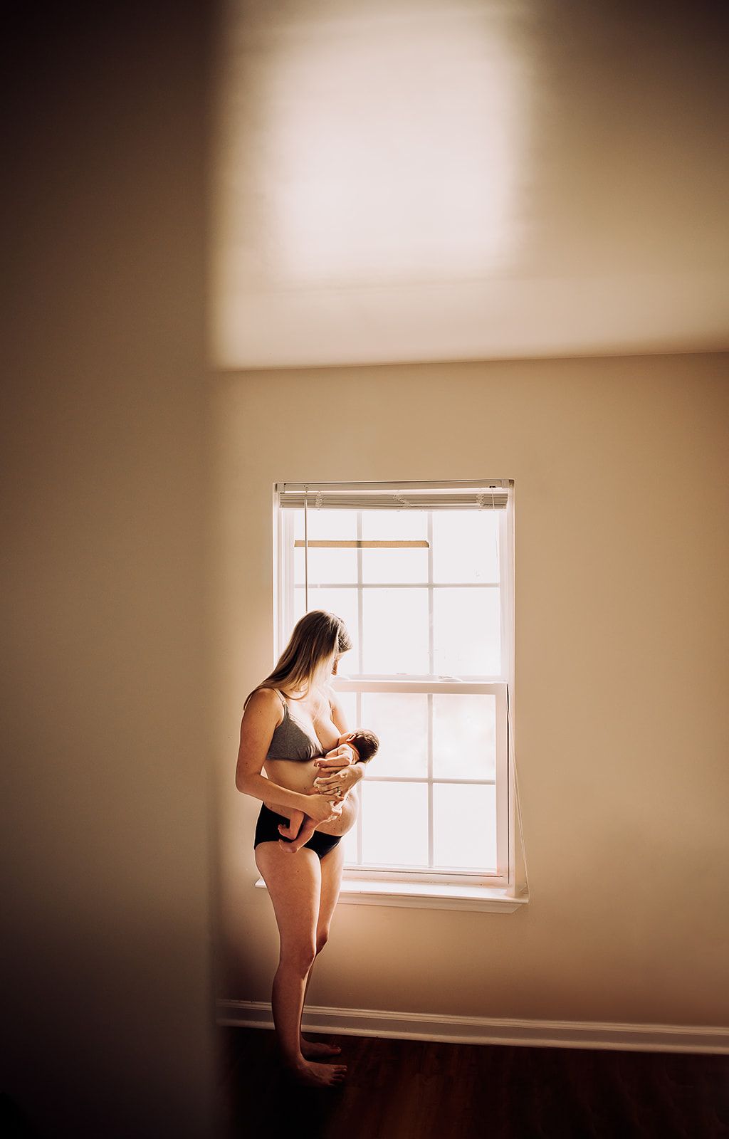 A new mother stands near a window nursing her newborn baby girl in her home a few days after birth.