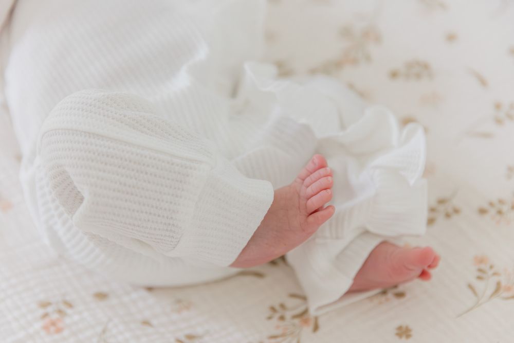 Newborn baby feet wrapped in a soft white knit blanket on a floral background.