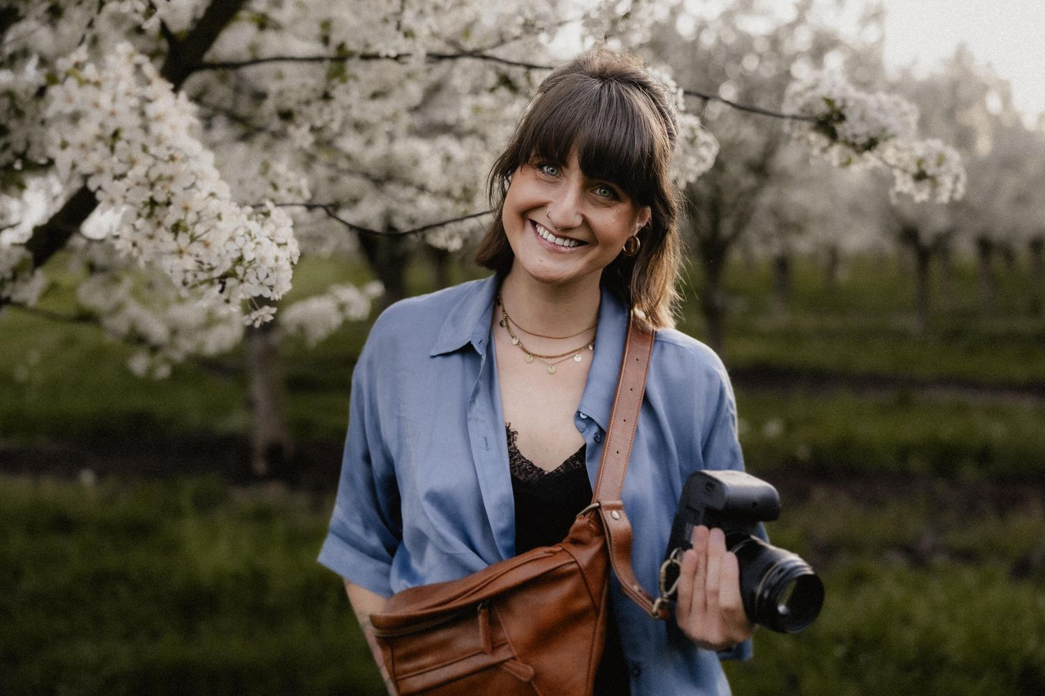 Photographer with camera bag poses near blooming cherry trees in spring.