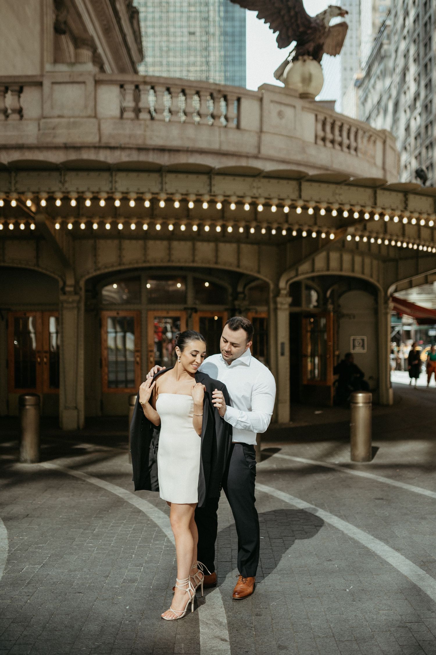 A couple shares a romantic moment under an ornate architectural archway with string lights.